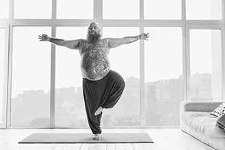Dickbäuchiger Mann mit Vollbart und tätowiertem Bauch macht Yoga